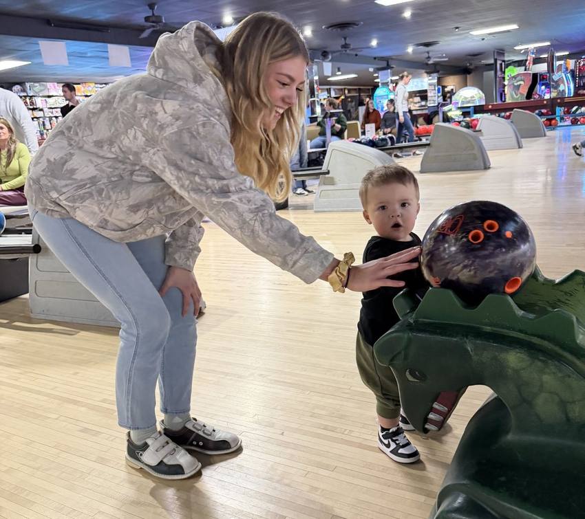 Mom helping a toddler roll a ball down the ramp