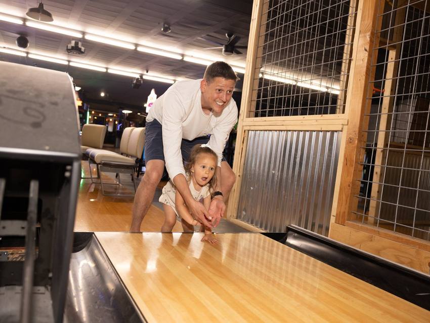 Dad and toddler rolling a duckpin ball